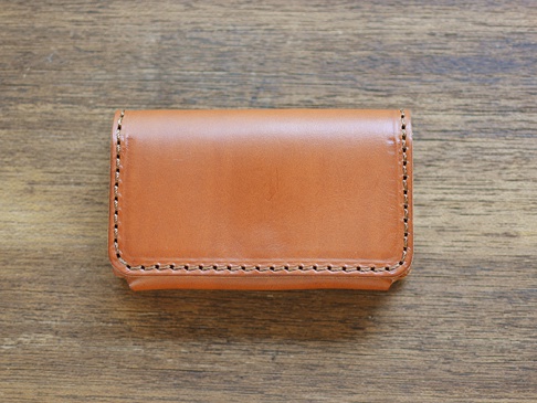 職人手作皮革Organ名片夾，顏色為淺棕色，材質為牛皮，邊緣有精緻的縫線，置於木紋背景上。