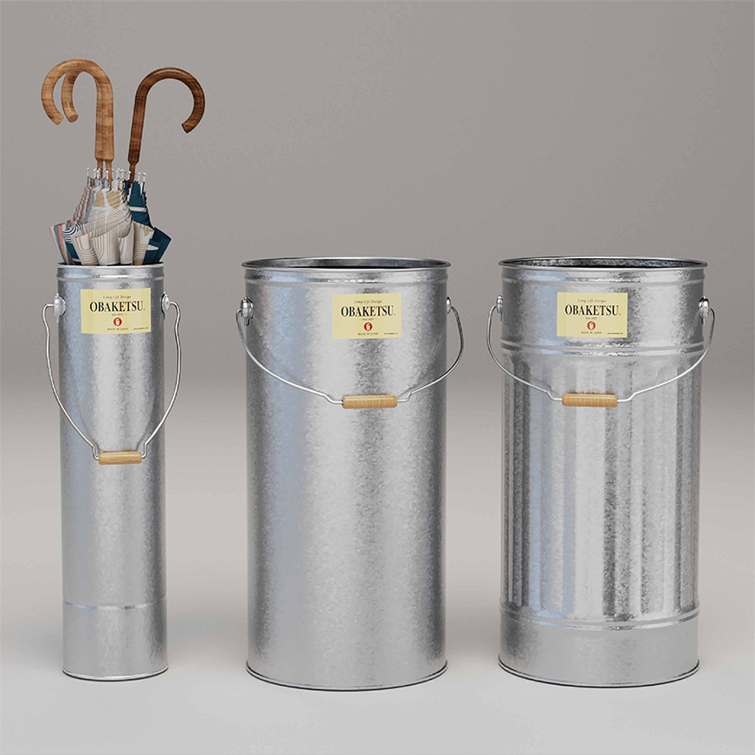 OBAKETSU 手工製傘桶，由三個不同尺寸的鍍鋅桶組成，其中左側的傘桶內插著幾把彩色的傘，兩個較大的傘桶側面均貼有 OBAKETSU 標籤，均配有木質提把。