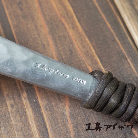 此圖片顯示鋁製湯勺的細節，湯勺柄部纏繞著深棕色繩結，上面刻有日文文字和「JAPAN」字樣。