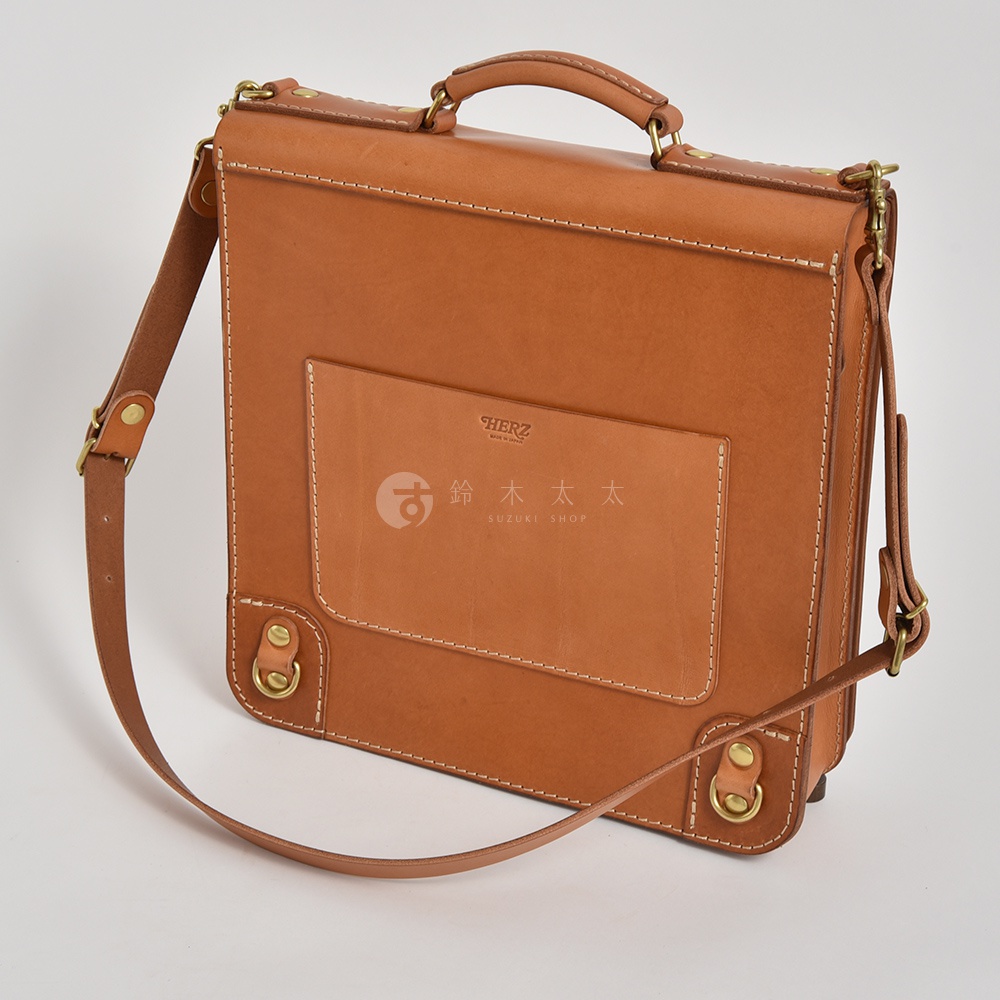 棕褐色皮革製成的手提後背包，設有三個外袋，可肩背或手提。包包上有「HERZ」及「SUZUKI SHOP」的品牌標誌。
