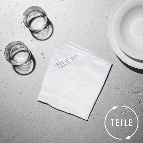 白色極吸水抗菌纖維擦拭巾，折疊平放在灰色檯面上，旁邊有兩個裝有水的玻璃杯和一個白色盤子。