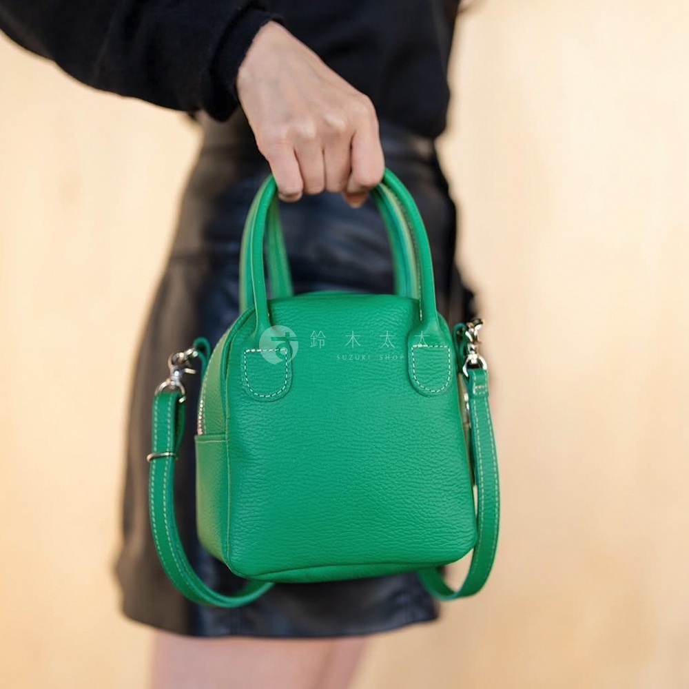 鮮綠色皮革手提單肩包，帶有頂部提手、可拆卸肩帶和銀色拉鍊。包身呈現貝殼狀，飾有對比色的白色縫線。