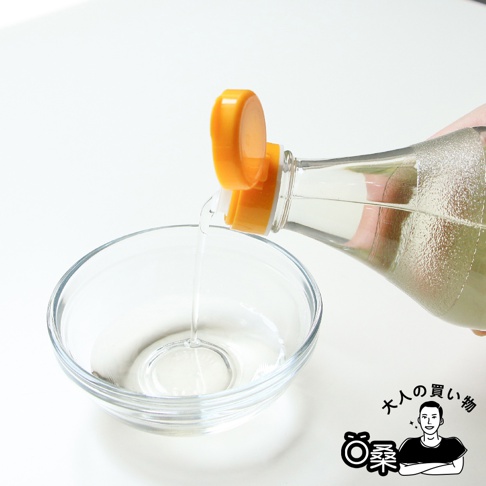 透明的米醋從橘色瓶蓋的透明玻璃瓶中傾倒至透明玻璃碗中。