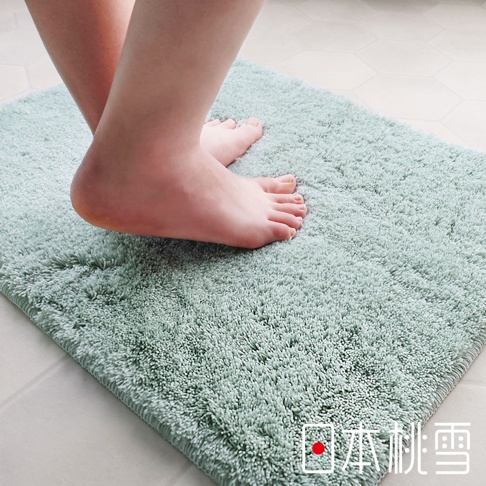 一雙赤腳踩在淺綠色的毛絨浴墊上，浴墊材質柔軟蓬鬆，後方可見部分地磚。