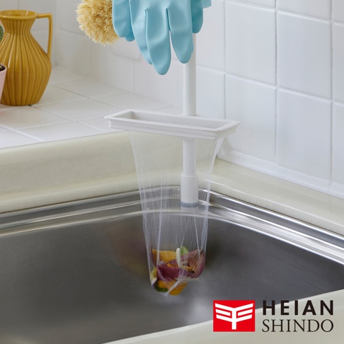 白色直撐款濾網架，架上掛著白色網袋，網袋中裝有廚餘，架子固定在廚房水槽邊緣。