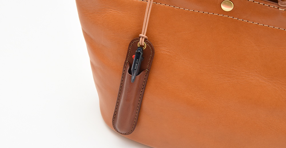 一個皮質筆套掛在一個棕色皮革包上，筆套裡插著一支黑色的筆。