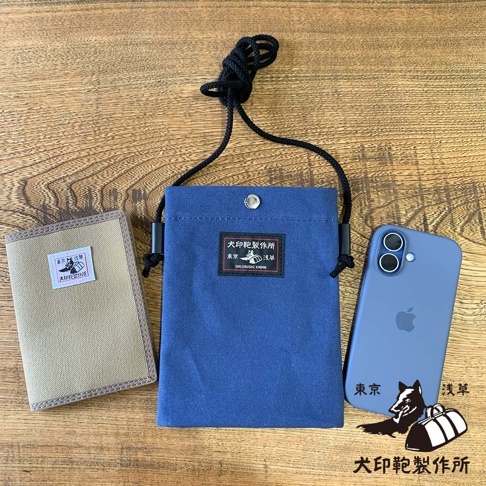 犬印鞄製作所藍色純綿帆布手機包，一旁放著卡其色帆布零錢包及一個手機殼