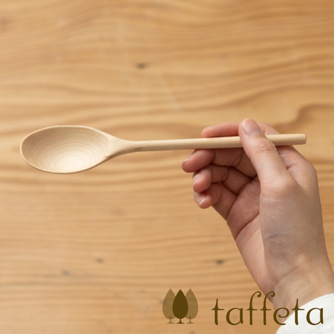 一隻手拿著一個淺色的楓木湯匙，湯匙呈現天然木紋，木勺部分呈橢圓形，手柄細長。