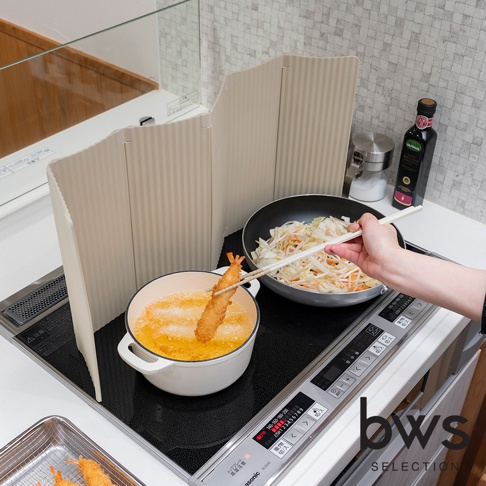 廚房IH爐旁，用筷子夾著剛炸好的天婦羅，鍋裡也炸著天婦羅，旁邊有菜餚和一瓶橄欖油，上方還有一個可摺疊的防油污隔板。