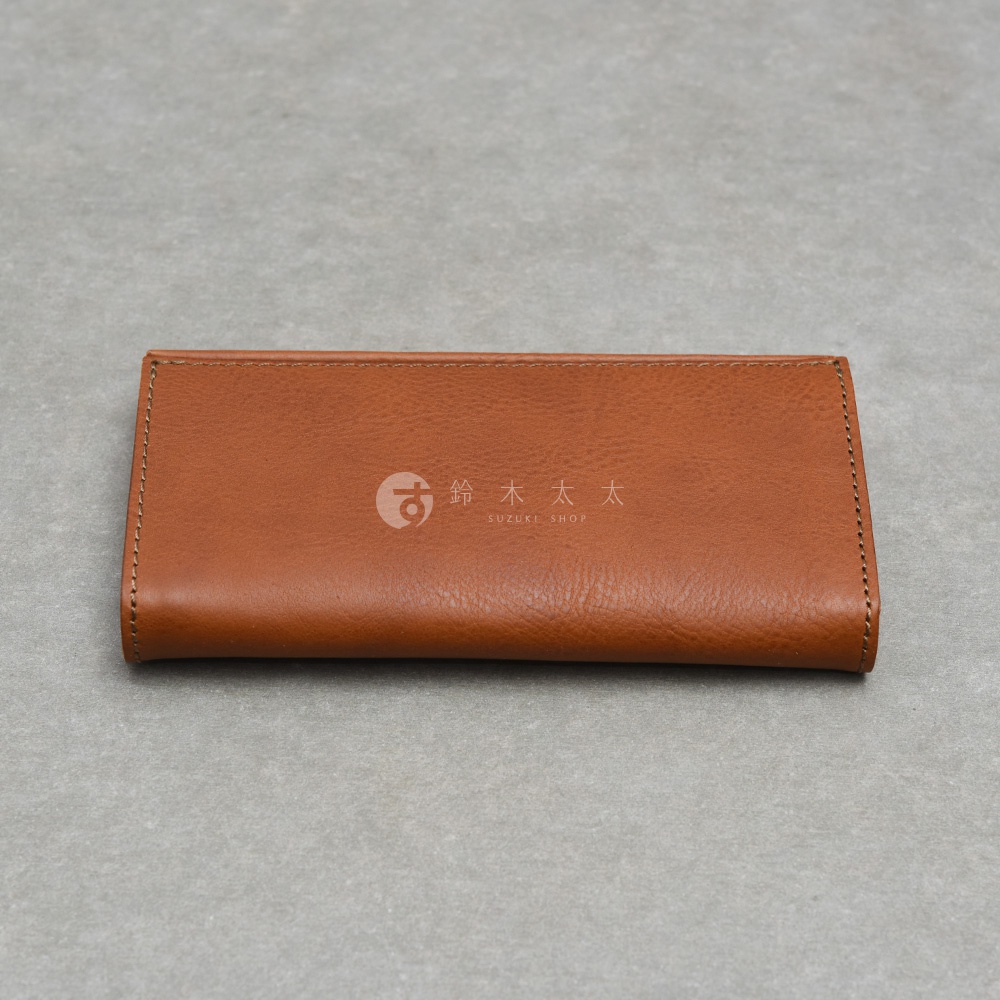一款棕色皮革長夾置於淺灰色背景上，長夾外觀簡約且表面有明顯的皮革紋理，上方印有鈴木太太 SUZUKI SHOP 的品牌標誌，整體呈現出職人手作的質感。