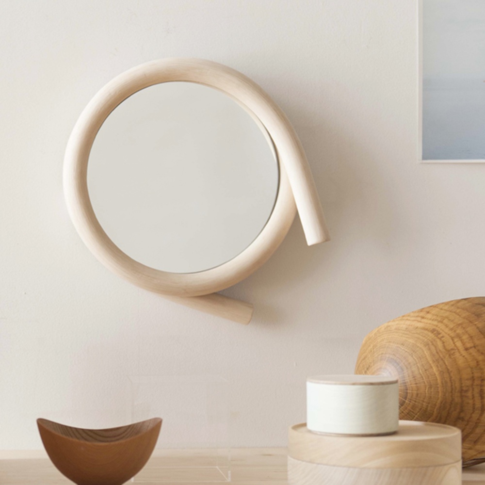 一個圓形鏡子，邊緣由淺色木質材料製成，呈現彎曲的線條，形成不規則的圓形外框。
