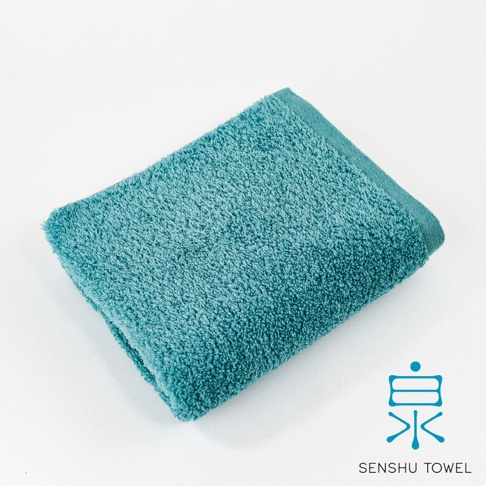 一條藍綠色長纖毛巾，觸感柔軟，毛圈蓬鬆，邊緣有簡約縫線。