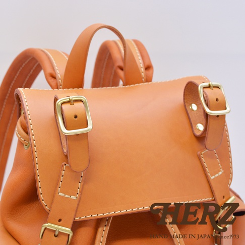 職人手作皮革復古風旅行後背包，呈現溫潤的淺棕色皮革，搭配黃銅色金屬扣環，縫線清晰，設計簡約大方。