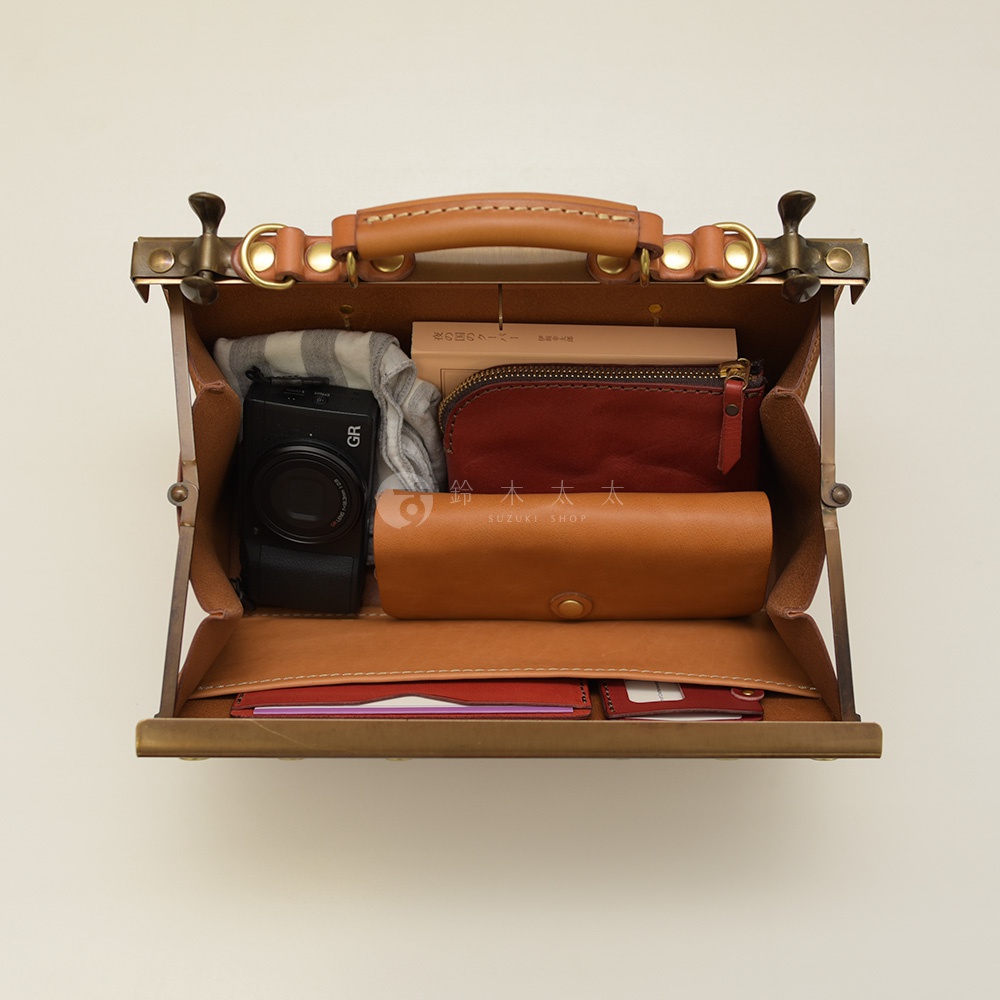 職人手作皮革復古口金兩用手提包 P-8，以焦糖色皮革製成，開口處設有復古金屬口金和皮革提把。包內裝有黑色相機、格紋圍巾、酒紅色化妝包、焦糖色皮革眼鏡盒，以及皮夾。