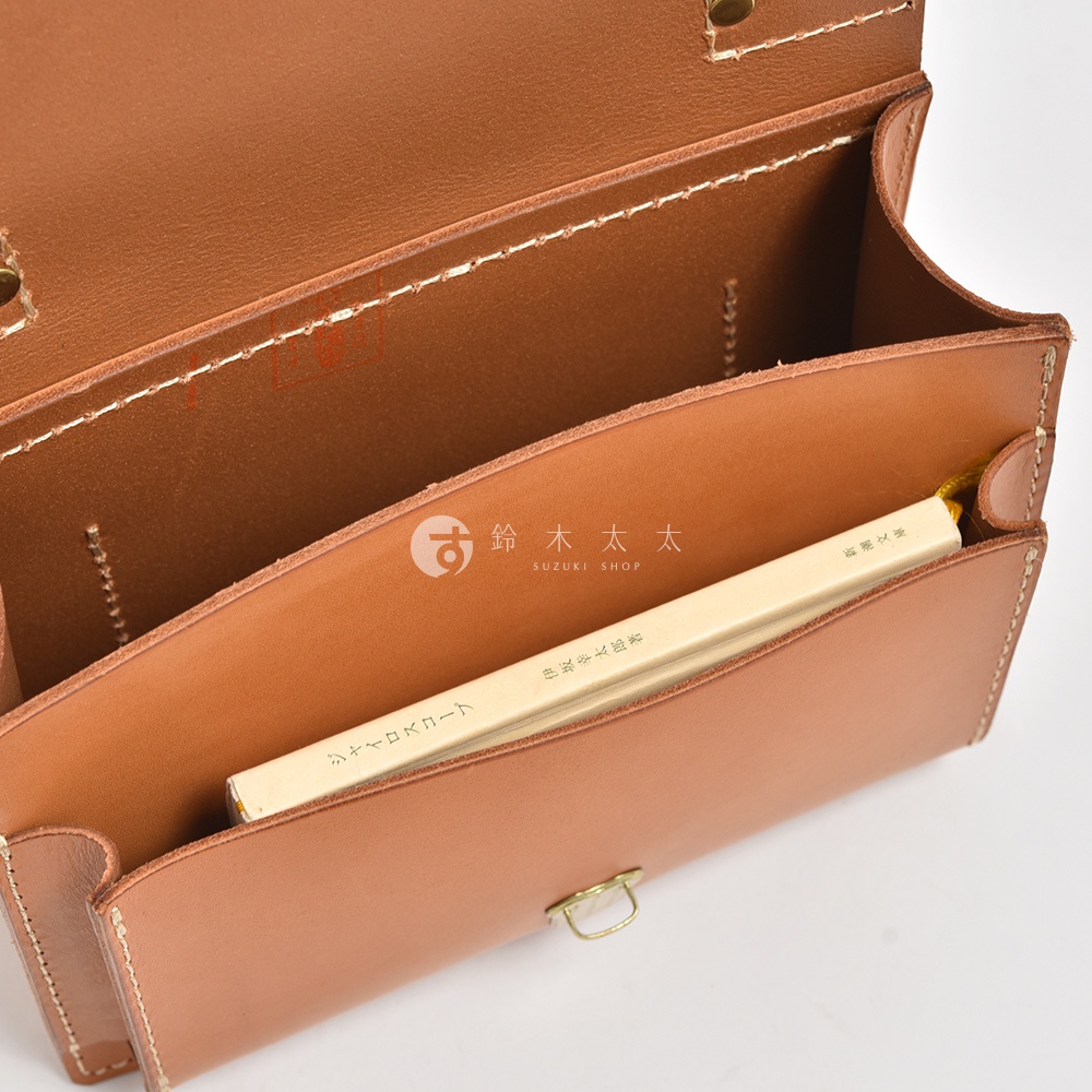 職人手作淺棕色皮革迷你單肩包，內側可見一本黃色封面書籍，包包以白色縫線裝飾，金屬扣環。