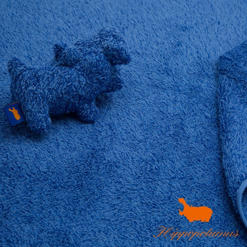 藍色竹棉混紡長毛巾，質地柔軟厚實，特寫畫面中可見一隻藍色絨毛小狗造型的填充玩具，其掛牌為橘色，另有品牌橘色河馬圖案與文字標誌。