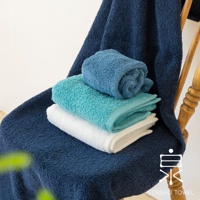 深藍色、藍綠色和白色浴巾疊放在椅子上，其中兩條浴巾捲起，展示了其柔軟的長纖維質地。