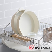 兩個淺米色圓形陶瓷不沾平底鍋堆疊在金屬瀝水架中，旁邊有兩個玻璃杯和一個木柄工具。