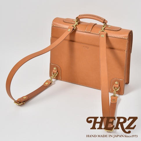 職人手作皮革三用單扣商務後背包，採用淺棕色皮革，搭配金色五金扣件，可見背包背部與可拆卸肩帶。