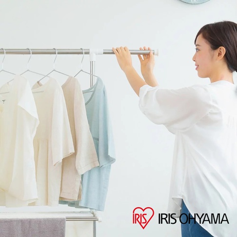 簡約不鏽鋼曬衣架，掛有四件不同顏色的棉麻質地衣物，包括白色、米色、淺棕色和淺藍色。一位女士正調整曬衣架的水平桿。