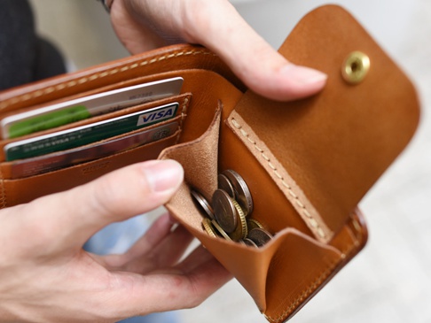職人手作皮革經典掀蓋扣式雙折短夾，棕色皮革材質，內有卡槽可插信用卡，零錢袋裝有數枚硬幣，掀蓋處有金色金屬釦。