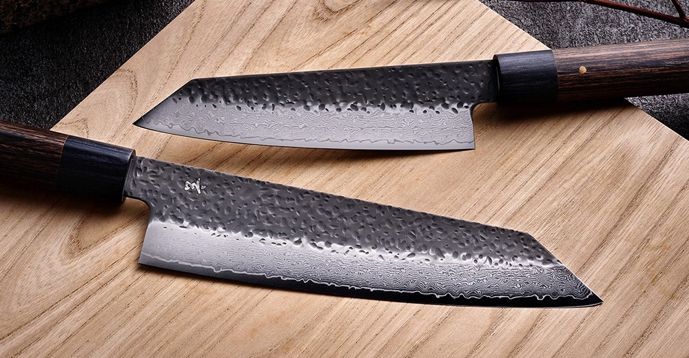 兩把日式廚刀，刀刃有錘紋和大馬士革鋼紋理，木質手柄，擺放在木質砧板上