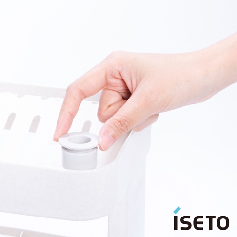 一隻手正將一個灰白色圓柱形組件插入白色三層收納架的頂部孔洞。收納架呈現淺米色，材質疑似塑膠，表面有細微顆粒。