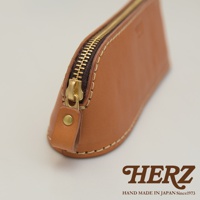 職人手作咖啡色皮革三角弧形收納筆袋，配有黃銅色拉鍊與金屬鈕扣，車縫線清晰可見。