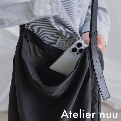 Atelier nuu ssent 肩背托特包，黑色尼龍材質，包身柔軟，側面內嵌手機袋，可放入手機，搭配條紋襯衫。