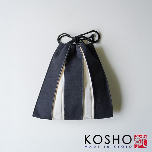 京都KOSHO品牌的一款ougi帆布信玄袋，外觀為深灰色與米白色相間的條紋設計，呈現出簡約的幾何風格，上方配有黑色束繩結，整體採用堅挺帆布材質製成，右下角印有KOSHO品牌標誌及紅色漢字印章。