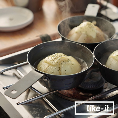 三個黑色金屬調理把手鐵杯，分別盛裝著水煮洋蔥，洋蔥頂部放有起司片並撒上香料，鐵杯置於爐架上，散發蒸氣。