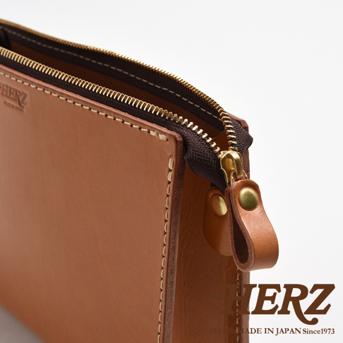 職人手作皮革三角底拉鍊手拿包，採用棕褐色皮革，搭配深棕色拉鍊及金色五金配件，側邊縫線清晰。
