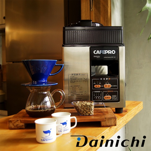 咖啡烘焙機 CAFEPRO MR-120，機身為銀色不鏽鋼材質，上方為黑色頂蓋。旁邊擺放有藍色濾杯、玻璃分享壺、兩只印有藍色標誌的白色咖啡杯，以及裝有生咖啡豆的小透明容器。