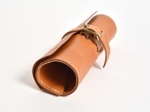 棕色皮革捲捲收納筆袋，附有皮帶及金屬扣環，邊緣縫線明顯。
