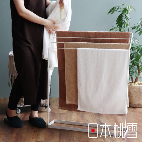 白色毛巾架上掛著四條飯店大毛巾，分別為深棕色、淺棕色、卡其色和白色，材質看起來柔軟厚實。