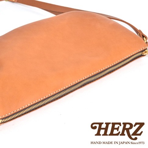 HERZ 職人手作皮革半圓馬鞍包，側面特寫，展示精緻縫線和拉鍊細節，下方印有品牌標誌。