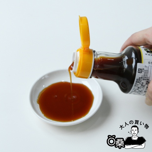 玻璃瓶裝森文柑橘醋調味料，黃色瓶蓋，深褐色液體正從瓶口倒入白色小碗中。