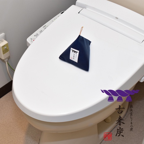 深藍色布製三角包，內含調濕木炭，布包上有白色標籤印有黑色日文，並以細繩懸掛。產品置於白色馬桶蓋上。