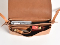 棕色皮革直式隨行袋，內部裝有錢包、手機和鑰匙串，以白色背景呈現。