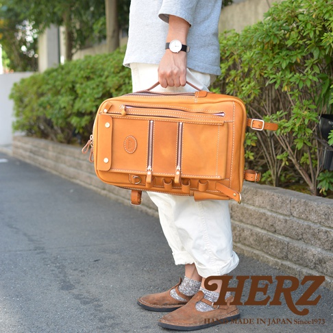 皮革製的棕褐色兩用後背包，有兩個前拉鍊袋，頂部有提把，肩帶隱藏在後方。