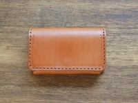 職人手作皮革Organ名片夾，顏色為淺棕色，材質為牛皮，邊緣有精緻的縫線，置於木紋背景上。