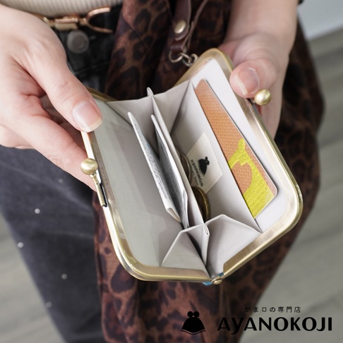 AYANOKOJI 品牌橫式口金卡片收納包，展示了打開的內部，可見卡片、零錢及標籤，由一雙手持握。