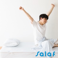 白色床墊上有一個淺藍色枕頭，一位穿著白色T恤的男子坐在床墊上伸展身體，身上蓋著一條藍白條紋的毛巾。