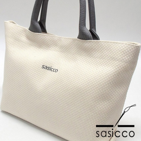 米白色三河木綿刺子織托特包，配有灰色提把，包身有「sasicco」字樣，底部右側有品牌標誌。