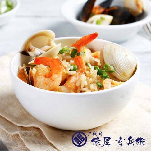 一碗盛滿米飯、鮮蝦、蛤蜊和青蔥的日式海鮮飯，米飯呈現金黃色，蝦子為粉紅色，蛤蜊為白色。