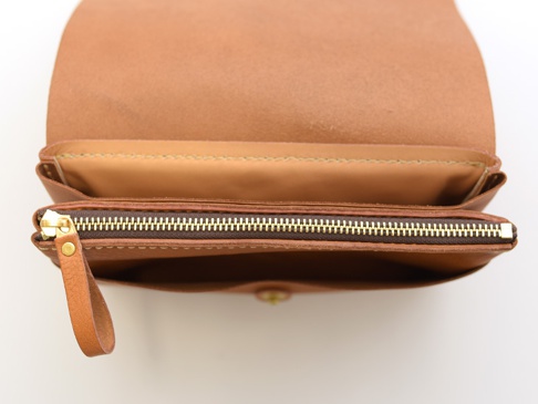 焦糖色皮革長夾，打開狀態，露出內層。左側有一個黃銅拉鍊，拉鍊頭附有皮革拉環。皮革邊緣縫線清晰可見。