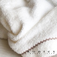 白色純棉連帽浴巾，質地柔軟蓬鬆，邊緣飾有淺棕色鋸齒狀滾邊，角落印有「kontex IMABARI JAPAN」字樣。