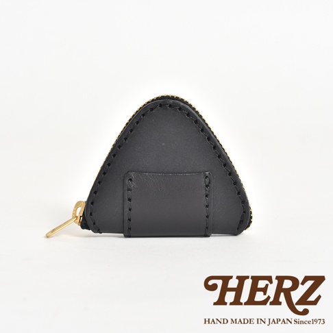 日本HERZ品牌職人手作黑色皮革零錢包，呈現可愛的三角飯糰造型，表面選用質地細膩的皮革製成，搭配精緻的金色拉鍊設計，底部並印有HERZ品牌標誌與產地資訊。