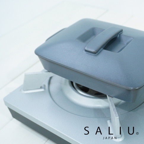 灰藍色陶製長方形烤盤，配有同色系帶提把的蓋子，放置於銀色爐具上。