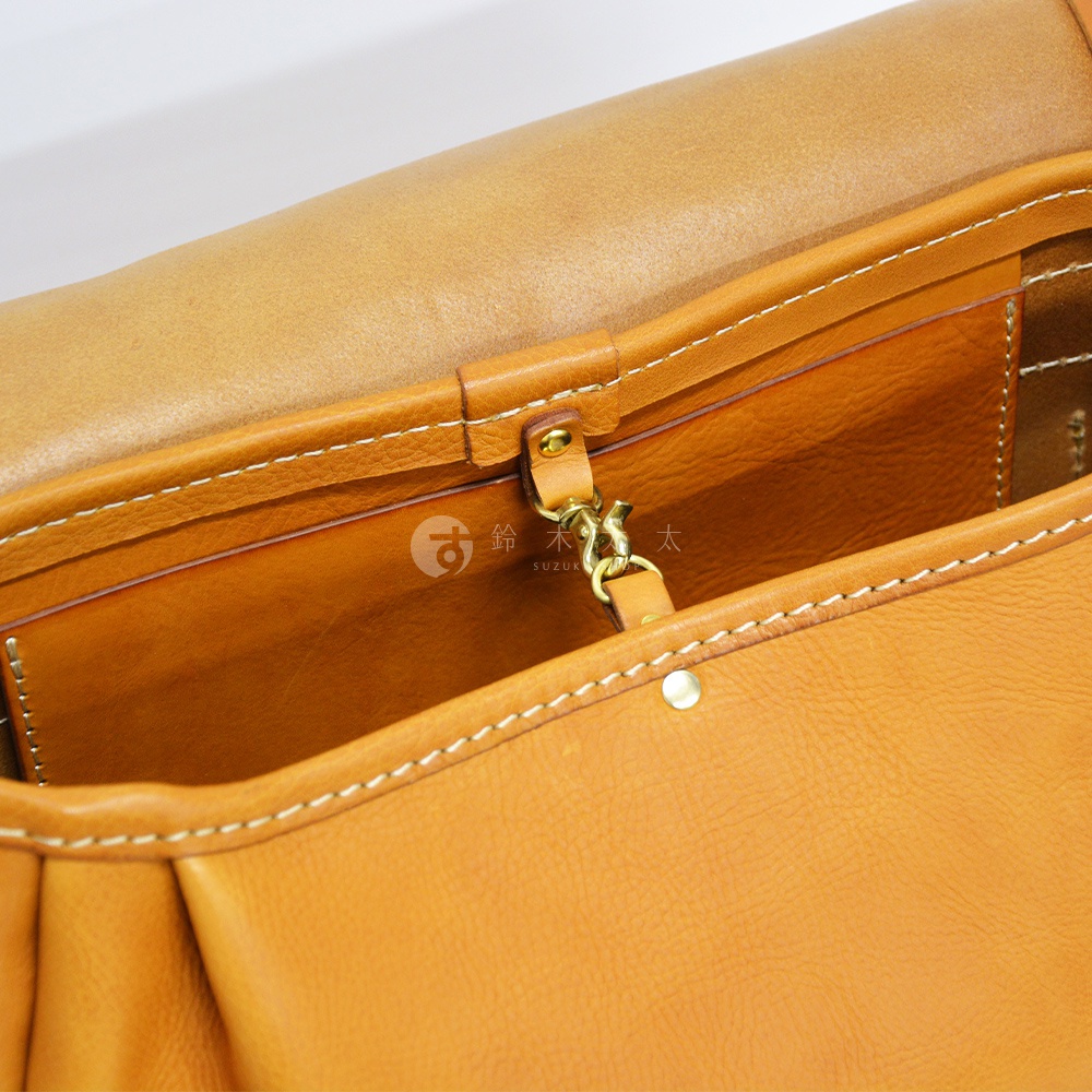 職人手作皮革復古翻蓋郵差包 CM-141，特寫展示包款內部，採用自然色澤的皮革材質，搭配白色車縫線與金色金屬扣環，展現細緻的工藝細節。